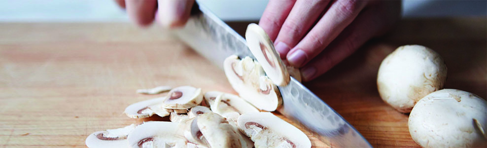 Fresh mushrooms being sliced on a wood cutting board.
