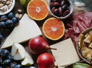 A lush cheese & charcuterie board with oranges, pistachios, salami and more.